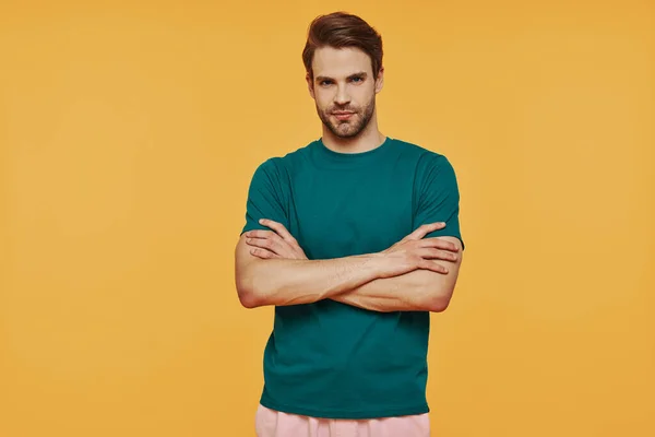 Bonito jovem em roupas casuais olhando para a câmera enquanto estava contra o fundo amarelo — Fotografia de Stock