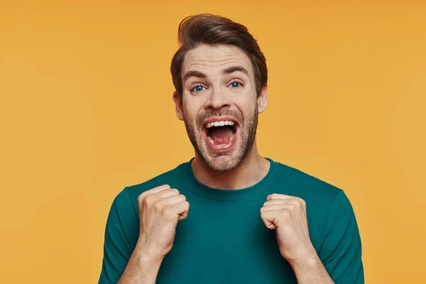 Bonito jovem sorrindo homem em roupas casuais olhando para a câmera e gesticulando — Fotografia de Stock