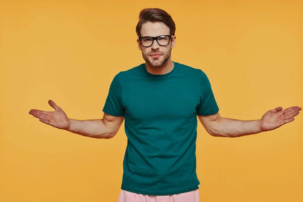 Knappe jongeman in casual kleding die naar de camera kijkt en armen uitgestrekt houdt — Stockfoto