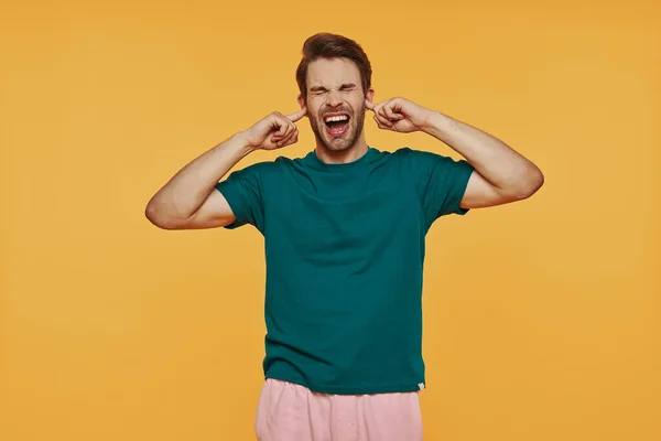 Jovem furioso em roupas casuais fazendo um rosto enquanto está de pé contra fundo amarelo — Fotografia de Stock