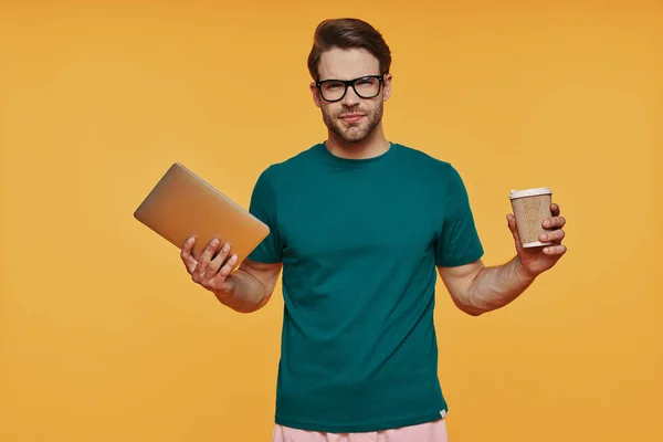 Bello giovane uomo in abbigliamento casual che trasporta tablet digitale e tazza — Foto Stock