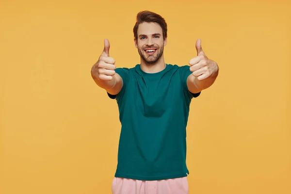 Stilig ung leende man i avslappnade kläder tittar på kameran och gester — Stockfoto