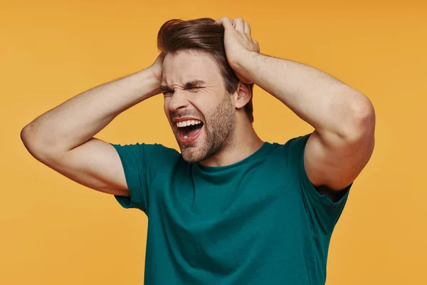 Portrait of frustrated young man holding head in hands and making a face — Stock Photo, Image