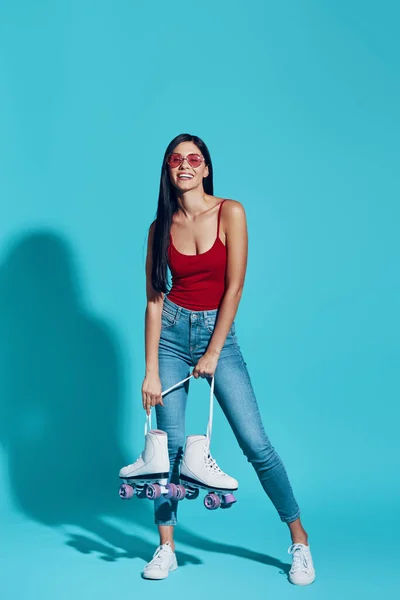 Full length of attractive young woman looking at camera and smiling while carrying roller skates — 图库照片