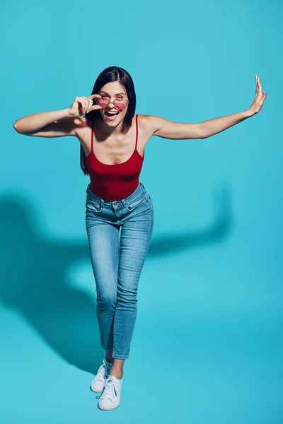 Full length of attractive young woman looking at camera and smiling while standing against blue background — Stock Photo, Image