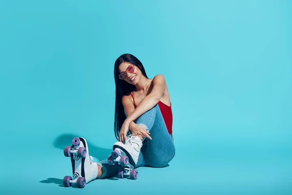 Atractiva joven mujer mirando a la cámara y sonriendo mientras usa patines sobre fondo azul — Foto de Stock