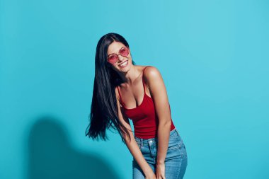 Çekici genç bir kadın mavi arka planda dururken kameraya bakıp gülümsüyor.