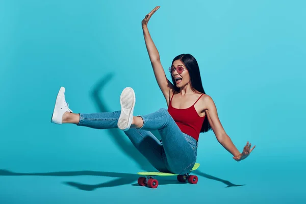 Giocoso giovane donna sorridente mentre skateboard contro sfondo blu — Foto Stock