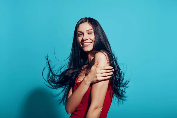 Attraktive junge Frau mit langen Haaren blickt in die Kamera und lächelt vor blauem Hintergrund — Stockfoto