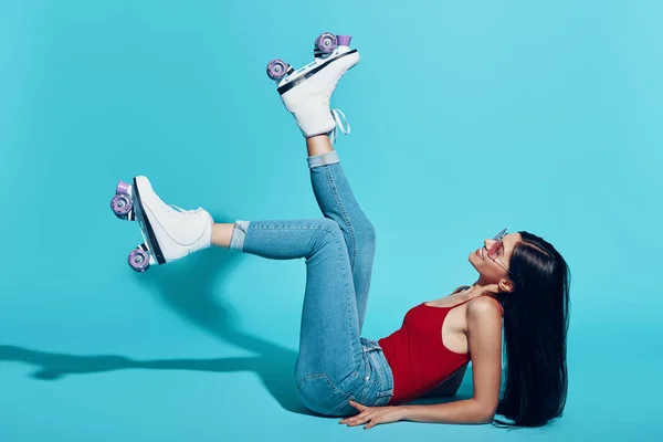 Attractive young woman wearing roller skates and smiling while lying against blue background — 图库照片