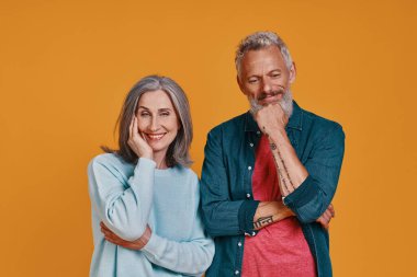 Turuncu arka planda yan yana dururken gülümseyen güzel yaşlı çift.