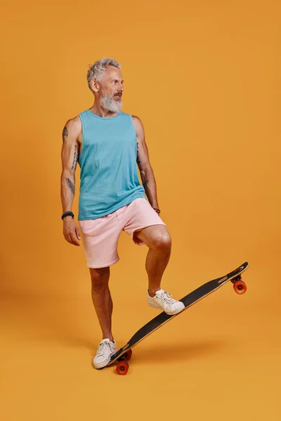Plná délka bezstarostný senior muž skateboarding při stání na oranžovém pozadí — Stock fotografie