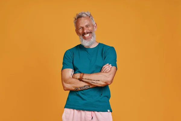Happy senior man looking at camera and smiling while standing against orange background — Stock Photo, Image