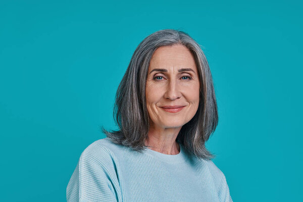 Фото зрелой красивой женщины, смотрящей в камеру и улыбающейся стоя на синем фоне