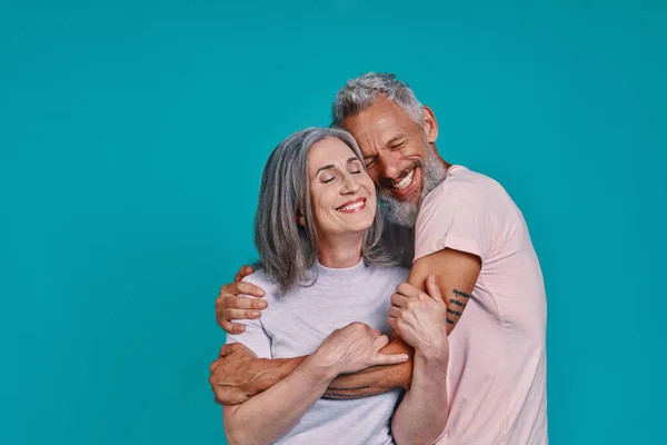 Älskande senior par bindning och leende när du står tillsammans mot blå bakgrund — Stockfoto