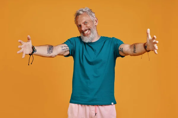 Happy senior man keeping arms outstretched and smiling while standing against orange background — Stock Photo, Image