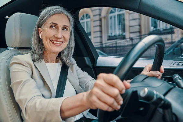 Mature belle femme en tenue décontractée intelligente souriant et conduisant assis sur le siège avant de la voiture — Photo
