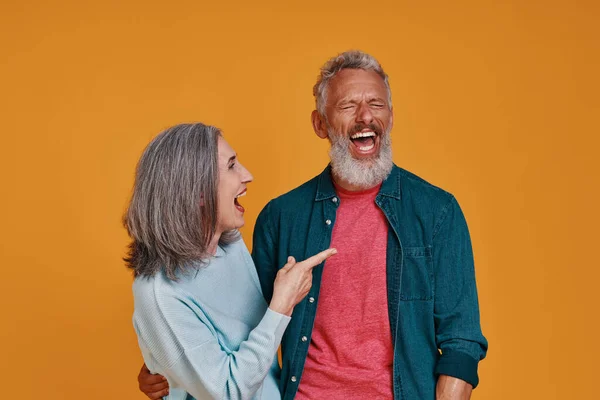 Beautiful senior couple laughing while standing together against orange background — Stock Photo, Image