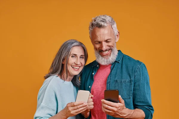Feliz pareja de ancianos sonriendo y usando teléfonos inteligentes y sonriendo — Foto de Stock