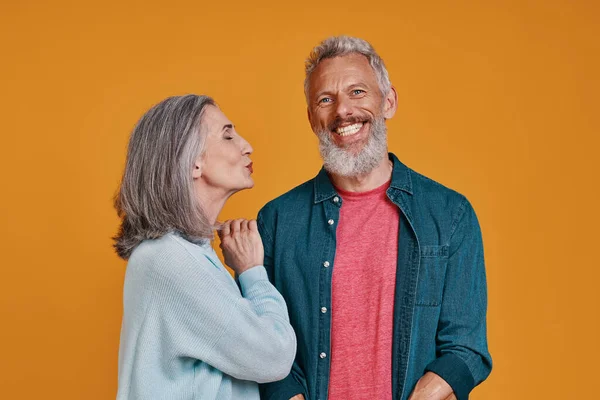 Beautiful senior couple smiling while standing together against orange background — Stock Photo, Image