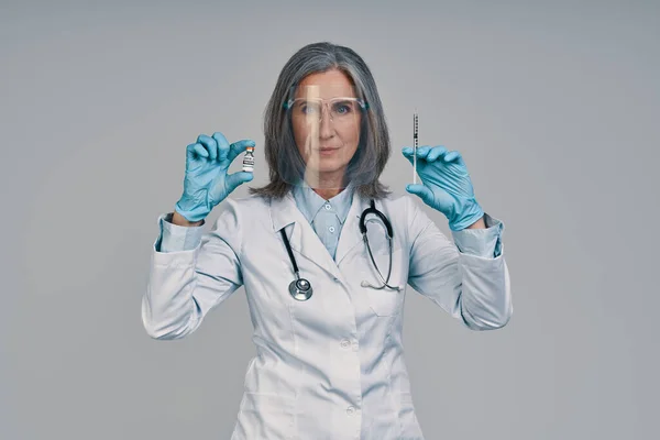 Rijpere mooie vrouwelijke arts in het gezicht schild houden spuit — Stockfoto