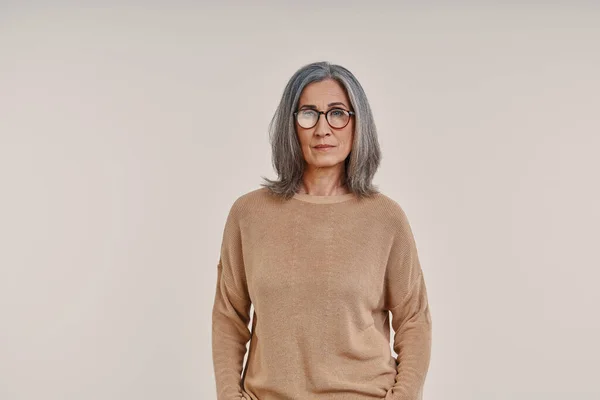 Reife schöne Frau schaut in die Kamera, während sie vor grauem Hintergrund steht — Stockfoto