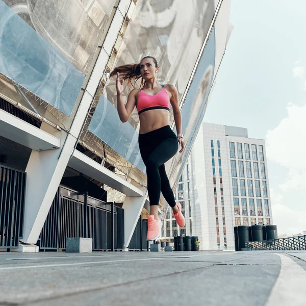 Comprimento total baixo ângulo vista de bela jovem mulher em roupas esportivas correndo ao ar livre — Fotografia de Stock