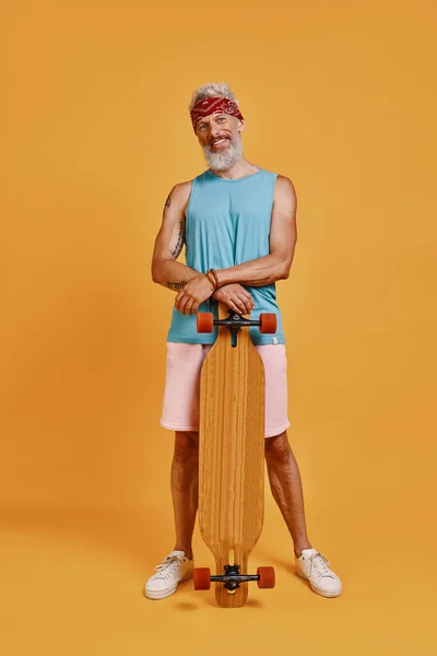 Полная длина активного пожилого человека, держащего скейтборд и улыбающегося — стоковое фото