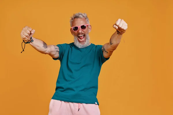 Elegante hombre mayor manteniendo los brazos extendidos y gritando mientras está de pie contra el fondo naranja — Foto de Stock