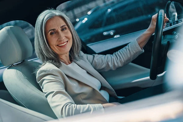 Mature belle femme en tenue décontractée intelligente regardant la caméra et souriant tout en conduisant la voiture — Photo