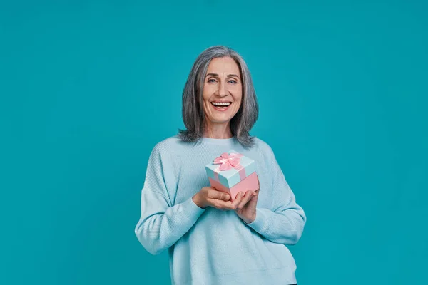 Mulher bonita madura olhando para a câmera e sorrindo enquanto está de pé contra o fundo azul — Fotografia de Stock