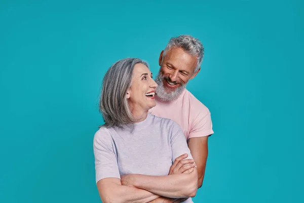 Gelukkig senior paar bonding en glimlachen terwijl staan samen tegen blauwe achtergrond — Stockfoto