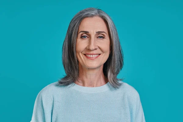 Kopfschuss einer reifen schönen Frau, die vor blauem Hintergrund in die Kamera blickt und lächelt — Stockfoto