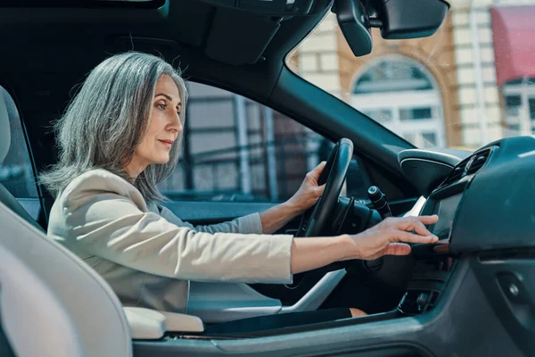 Mulher bonita madura em desgaste casual inteligente usando o sistema de posicionamento global durante a condução de carro — Fotografia de Stock