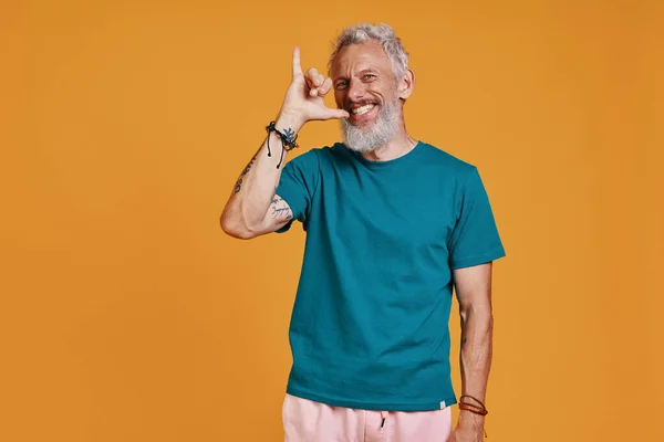 Hombre mayor despreocupado haciendo gestos y sonriendo mientras está de pie sobre fondo naranja — Foto de Stock