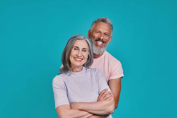 Beau couple de personnes âgées regardant la caméra et souriant tout en se tenant ensemble sur fond bleu — Photo