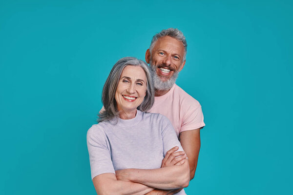 Beautiful senior couple looking at camera and smiling while standing together against blue background