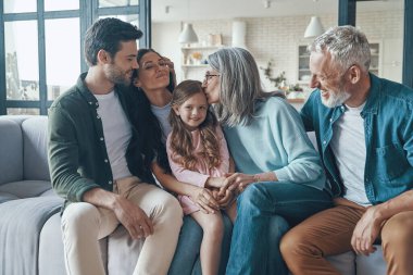 Mutlu bir aile birlikte vakit geçirir ve evdeki kanepede otururken gülümser.