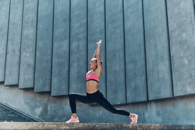 Spor elbiseli, kendine güvenen genç bir kadın. Açık havada esneme egzersizleri yapıyor.