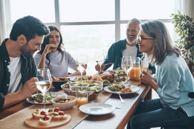 Mutlu çoklu nesil aile yemeği yerken iletişim kuruyor ve gülümsüyor.