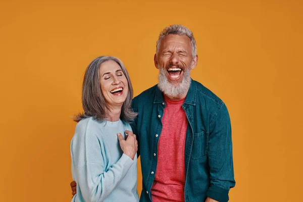 Beautiful senior couple laughing while standing together against orange background — Stock Photo, Image