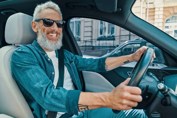 Heureux homme âgé en vêtements décontractés profiter de balade en voiture tout en étant assis sur le siège avant de la voiture — Photo