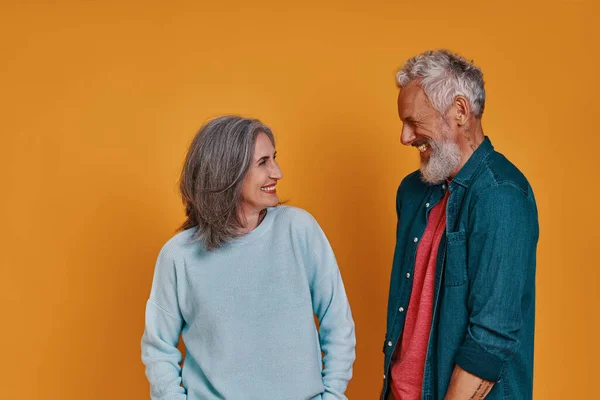 Vackra senior par tittar på varandra och ler när de står tillsammans mot orange bakgrund — Stockfoto