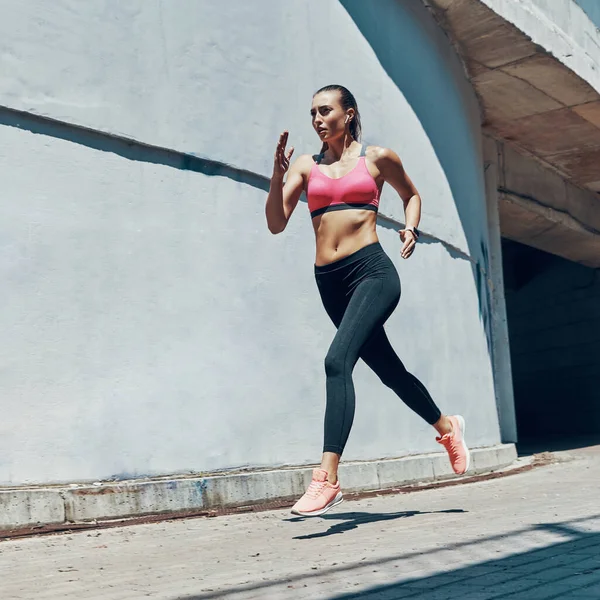 Comprimento total de bela jovem mulher em roupas esportivas correndo ao ar livre — Fotografia de Stock