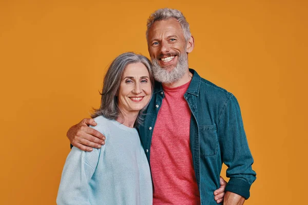 Romantiskt äldre par tittar på kameran och ler när de står tillsammans mot orange bakgrund — Stockfoto