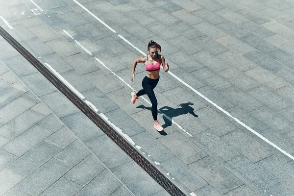 Вид сверху привлекательной молодой женщины в спортивной одежде, бегущей по улице — стоковое фото
