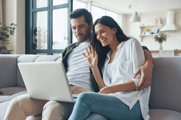 Bella coppia giovane bere caffè e guardando sul computer portatile mentre seduto sul divano a casa — Foto Stock