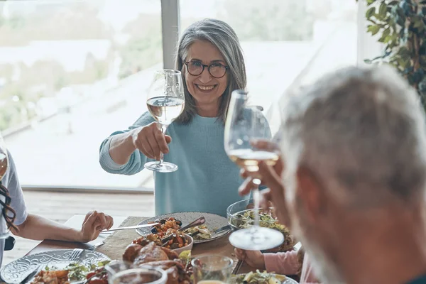 Feliz pareja de ancianos brindando entre sí y sonriendo mientras cenan juntos entre la familia — Foto de Stock