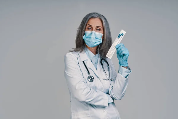 Mature beautiful female doctor in face mask looking at camera and holding medical test — Stock Photo, Image