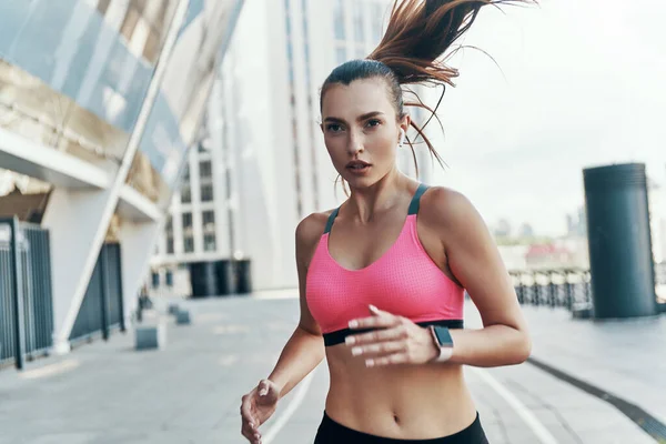 Συμπυκνωμένη νεαρή γυναίκα με αθλητικά ρούχα φορώντας τρέξιμο σε εξωτερικούς χώρους — Φωτογραφία Αρχείου